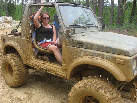 1987 Suzuki Samurai - A woman sits in a heavily mud-covered Suzuki Samurai, ready for an off-road adventure.