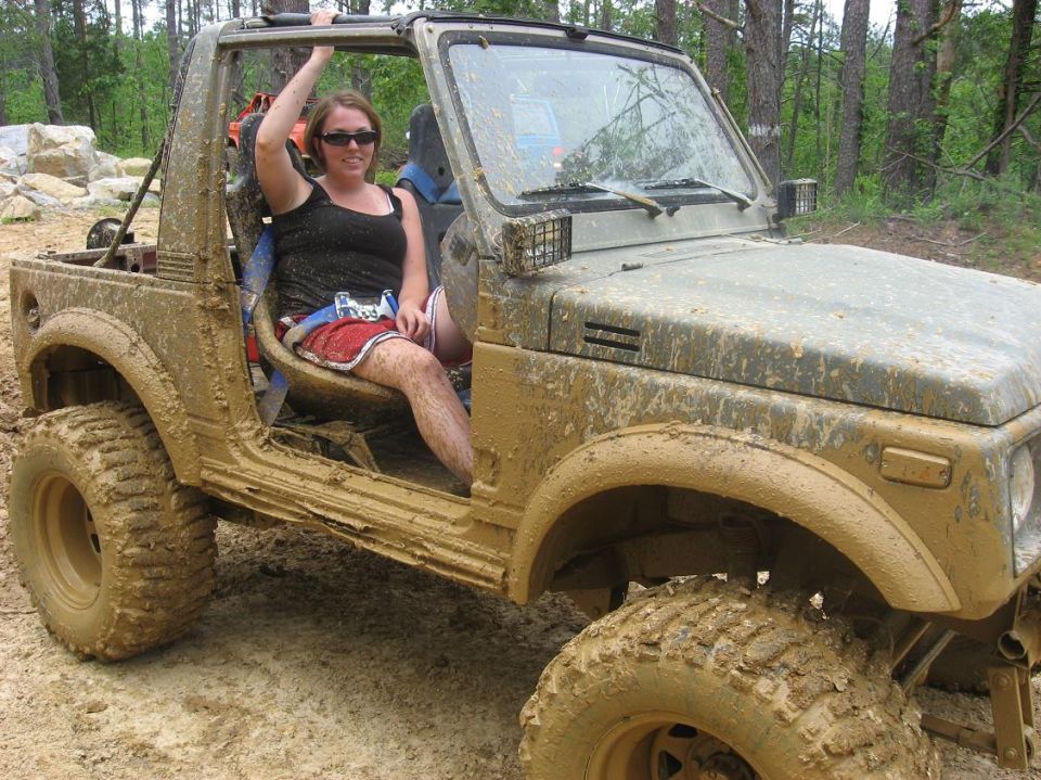 Muddy Suzuki Samurai with a woman in the driver's seat, off-roading