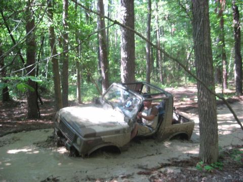 1987 Suzuki Samurai - A Suzuki Samurai navigates a muddy trail through a dense forest.
