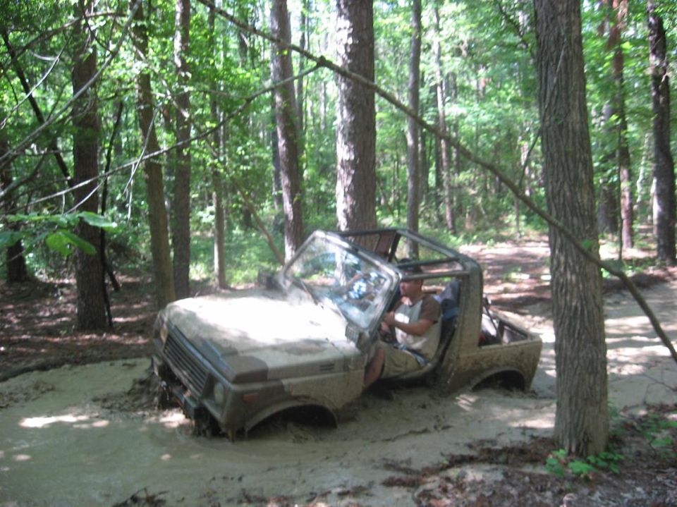 Camouflaged Suzuki Samurai stuck in mud, front-left wheel submerged