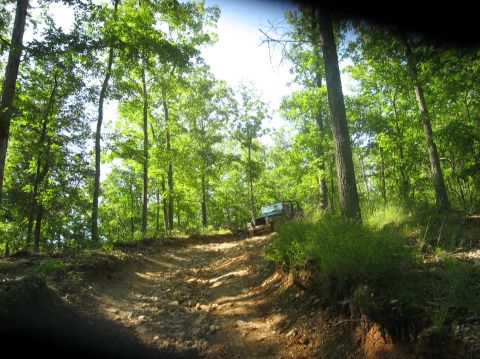 1987 Suzuki Samurai - Off-road vehicle navigates a challenging dirt trail surrounded by dense green trees.