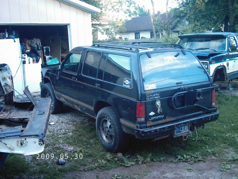 1994 GMC Jimmy - A black 1994 GMC Jimmy SUV is parked in a grassy area next to a garage, with another vehicle visible in the background.