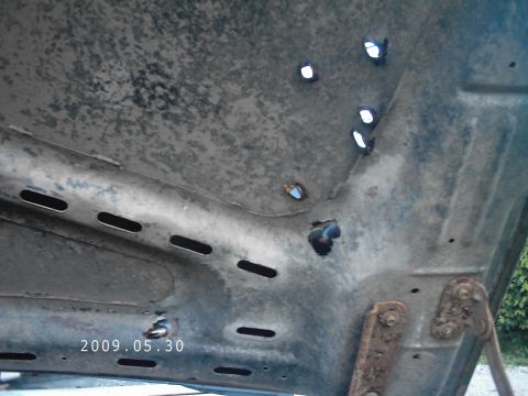 1986 Ford Bronco - The underside of a vehicle hood shows signs of wear and tear, with multiple holes and rust visible.