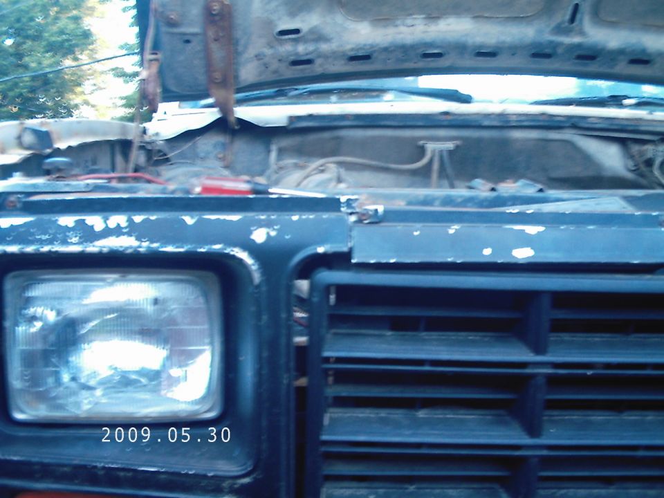 Front grille and headlight of a dark blue vehicle with hood open. Date 2009.05.30 visible