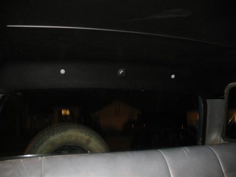 1992 Ford Bronco - Dark interior view looking rearward through the back window of a vehicle, showing the headliner with three round dome lights or fasteners a…