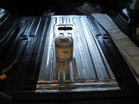 1992 Ford Bronco - Interior floor pan of a vehicle covered with reflective self-adhesive sound-deadening/insulation mat, with a can of 'Peel & Seal' roll prod…