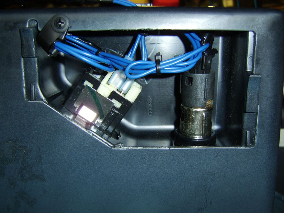 Console cavity with blue wires, white connector, and chrome power socket in gray plastic trim