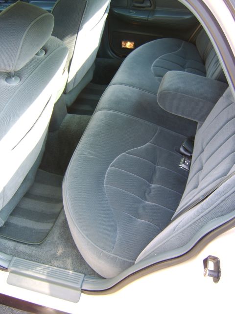1996 Mercury Grand Marquis - Interior view of the rear bench seat in a sedan, upholstered in dark gray/blue cloth, viewed through an open rear door. The gray carpet, do…