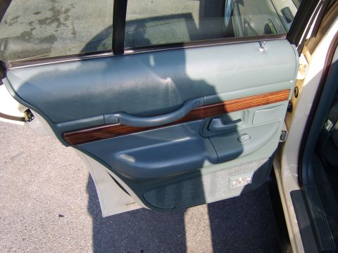 1996 Mercury Grand Marquis - Interior view of a rear door panel on a light-colored sedan, showing sage-green upholstery with a wood-grain accent trim, integrated armres…