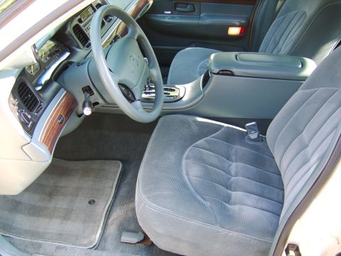 1996 Mercury Grand Marquis - Interior view of a sedan from the driver's side, showing a gray cloth front bench seat, center console, and steering wheel with faux wood d…