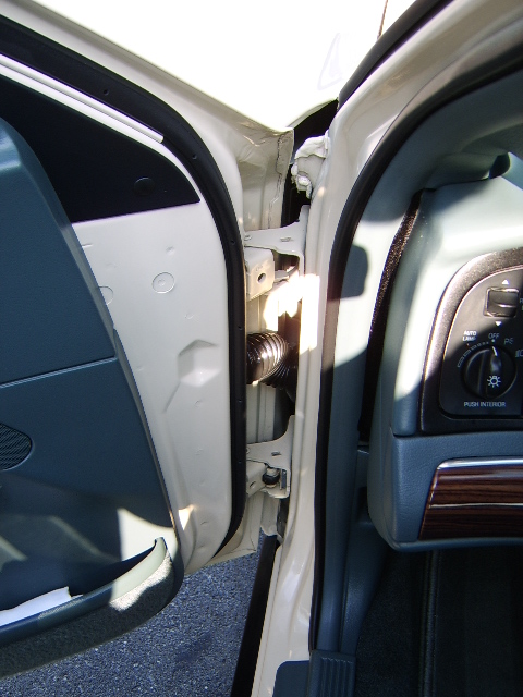 1996 Mercury Grand Marquis - Close-up of an open driver's door jamb on a tan/cream sedan, showing the door hinge, spring mechanism, and body-side sill; the interior doo…