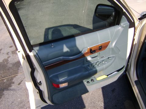 1996 Mercury Grand Marquis - Interior view of the front driver's door panel on a white sedan, showing gray leather trim with faux wood-grain accents, chrome window and…