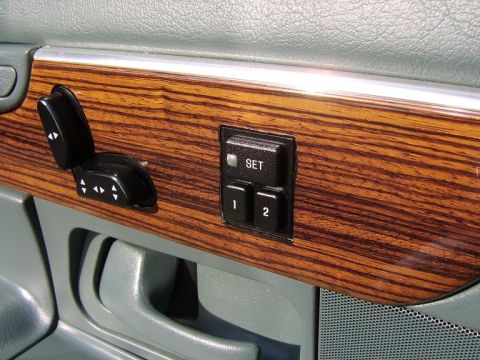 1996 Mercury Grand Marquis - Close-up of a door panel with wood-grain trim showing black seat/memory controls, including seat adjustment switches and memory buttons lab…