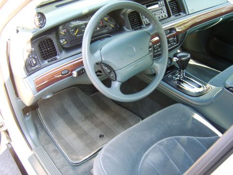 1996 Mercury Grand Marquis - Interior view of a Mercury sedan showing the gray steering wheel with Mercury logo, matching gray dashboard with woodgrain trim, analog gau…