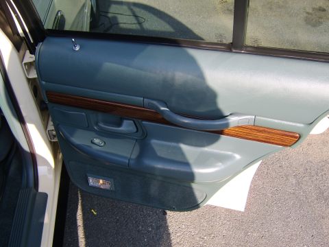 1996 Mercury Grand Marquis - Interior view of a rear door panel in gray/sage two-tone upholstery with a wood-grain accent trim strip, molded armrest, door pull handle,…