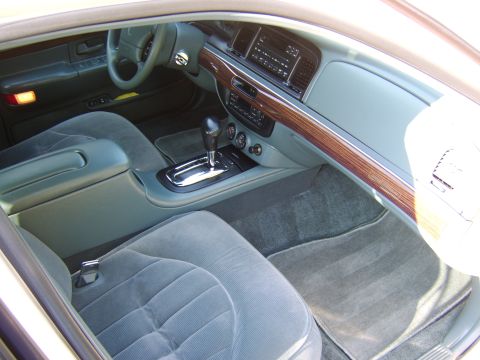 1996 Mercury Grand Marquis - Interior view of a gray-upholstered sedan shot through the passenger door, showing the front cabin with cloth seats, center console with fl…