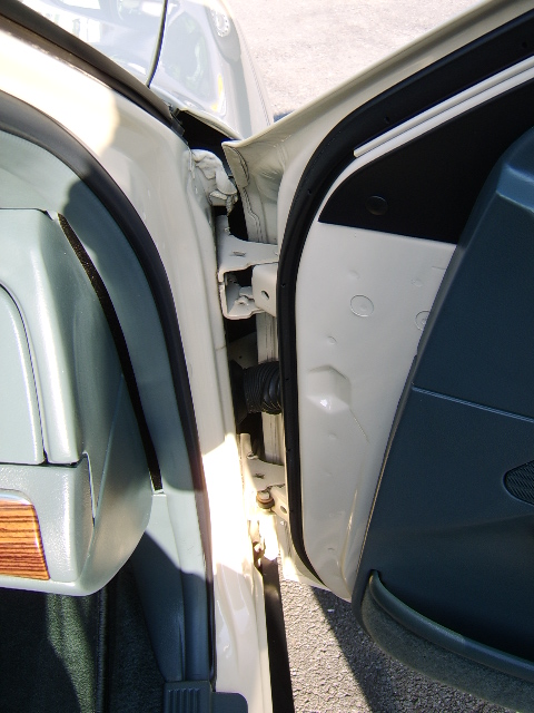 1996 Mercury Grand Marquis - Close-up of an open car door on a cream/tan sedan, showing the front door hinge area, door jamb, weatherstripping, and a corner of the inte…