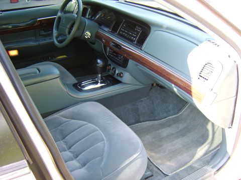 1996 Mercury Grand Marquis - Interior view of a gray/blue cabin shot from the open passenger door, showing the dashboard, wood-grain trim, floor-mounted shifter, cloth…