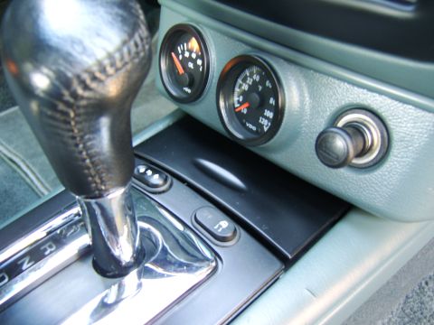 1996 Mercury Grand Marquis - Interior center console close-up showing a leather-wrapped automatic shifter with chrome trim, plus two aftermarket VDO gauges (oil pressur…