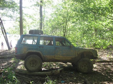 1987 Suzuki Samurai - Jeep Cherokee XJ navigates a wooded trail, tires covered in mud.