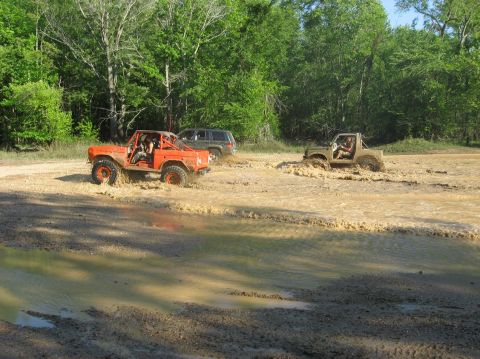 1987 Suzuki Samurai - Multiple off-road vehicles navigate a muddy terrain with trees in the background.