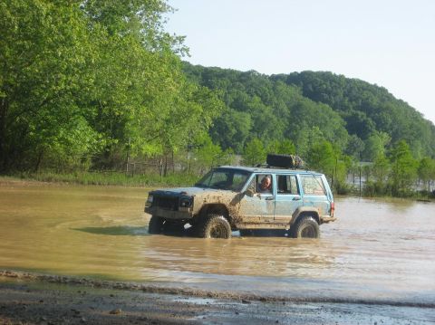 1987 Suzuki Samurai - Jeep Cherokee XJ navigates through a muddy water obstacle during an off-road excursion.