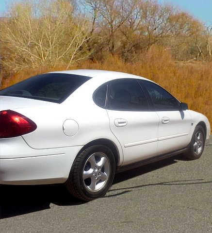 2000 Ford Taurus - A white 2000 Ford Taurus is viewed from the side, parked outdoors with a natural landscape behind it.