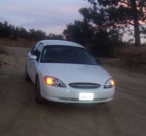2000 Ford Taurus - White 2000 Ford Taurus parked on a dirt road with trees in the background.