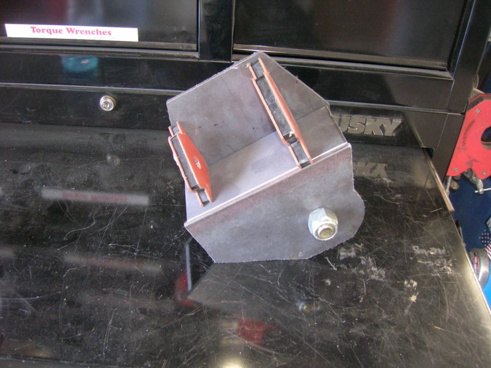 Custom metal bracket with bolt and rubber inserts, sitting on a scratched workbench