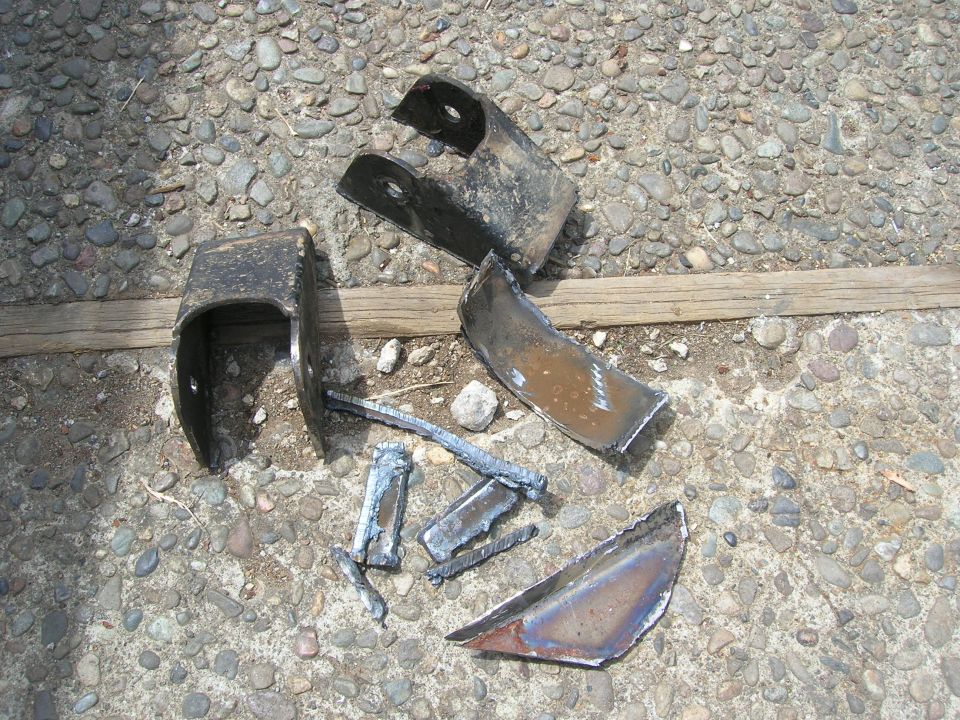 Pile of broken metal brackets and pieces on a gravel surface