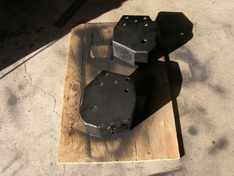 1996 Ford Bronco - Two freshly painted black metal radius arm mounts rest on a wooden board.