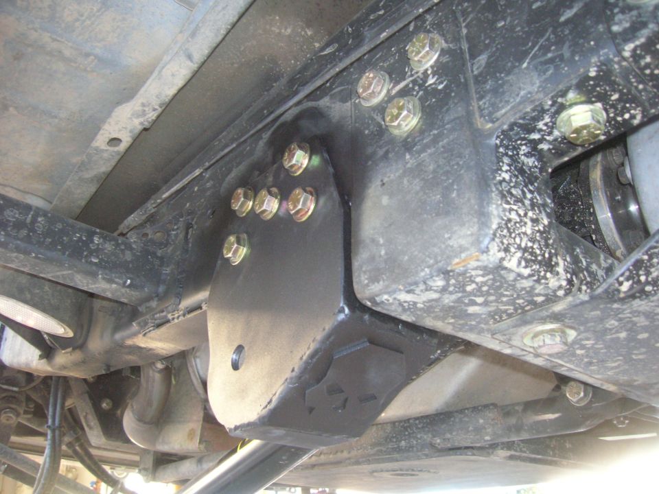 Underside of vehicle frame showing a newly installed metal bracket bolted to the chassis, likely for suspension modification