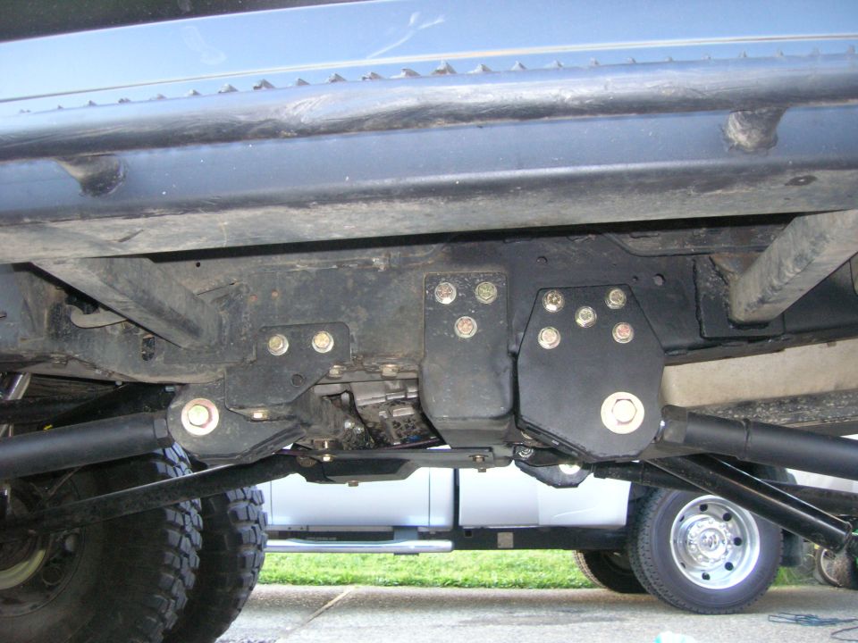 Aftermarket radius arm mounts on a vehicle's underbody, with another truck visible in the background