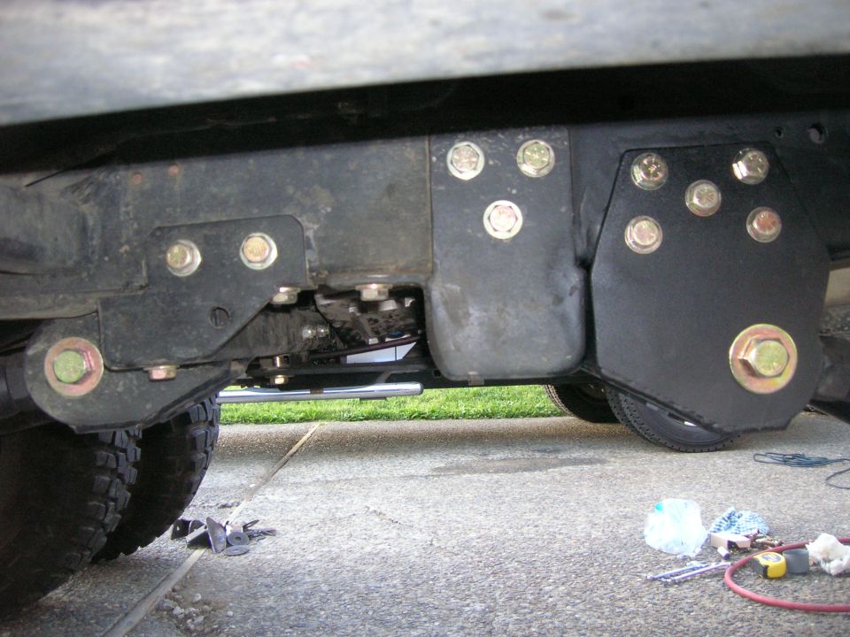 Close-up of a custom bracket bolted to a vehicle's frame near the rear tire