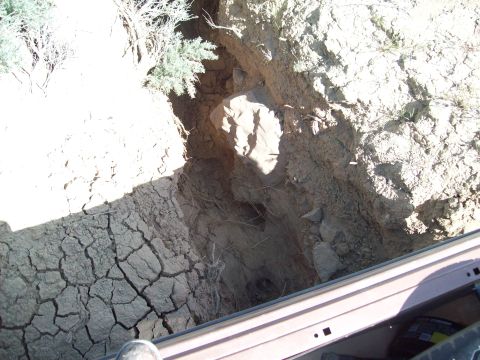 1985 Ford Bronco - A dry, cracked earth ditch with some vegetation, seen from the perspective of a vehicle.