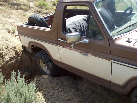 1985 Ford Bronco - This classic Ford Bronco is navigating a challenging off-road terrain, getting stuck in a deep rut.