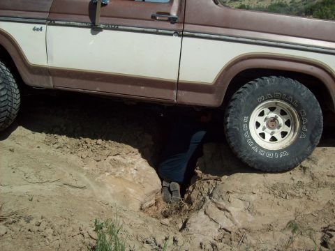 1985 Ford Bronco - A person works on a Ford Bronco stuck in a ditch, with its side visible.