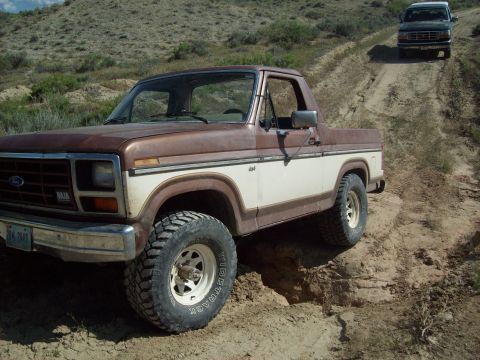 1985 Ford Bronco - A 1985 Ford Bronco navigates a dusty trail, with another vehicle following behind.