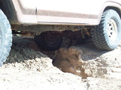 1985 Ford Bronco - Vehicle navigating difficult off-road terrain, showing undercarriage and tires.