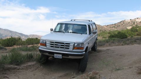 1996 Ford C-350 (Centurion Conversions) - A white Ford Bronco is parked on a dirt path with a mountainous landscape behind it.
