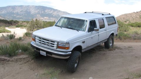 1996 Ford C-350 (Centurion Conversions) - White Ford SUV with aftermarket wheels on a dirt road, with mountains in the background.