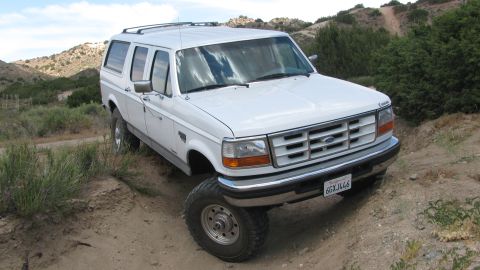 1996 Ford C-350 (Centurion Conversions) - This white SUV is on a dirt road with hills in the background.