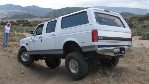 1996 Ford C-350 (Centurion Conversions) - A white 1996 Ford C-350 Centurion Conversions SUV is shown in a desert landscape, lifted with large off-road tires.