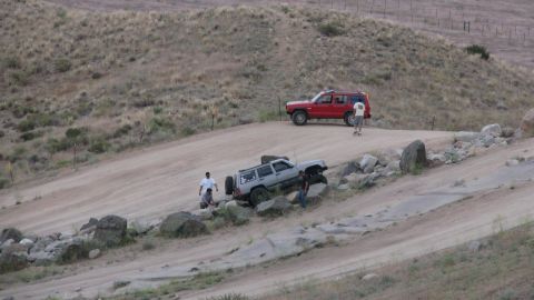 1996 Ford C-350 (Centurion Conversions) - Two SUVs are seen off-roading on a rocky dirt track with dry grass hills in the background.