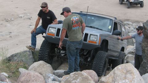 1996 Ford C-350 (Centurion Conversions) - Modified Jeep Cherokee XJ is being driven over rocks with assistance from onlookers.