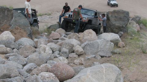 1996 Ford C-350 (Centurion Conversions) - Several off-road vehicles tackle a challenging rocky terrain, with people assisting.