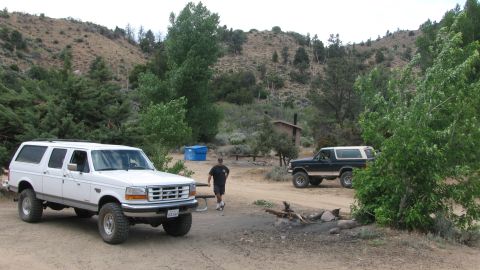 1996 Ford C-350 (Centurion Conversions) - Two SUVs are parked at a campsite in a dry, hilly area with scattered trees.