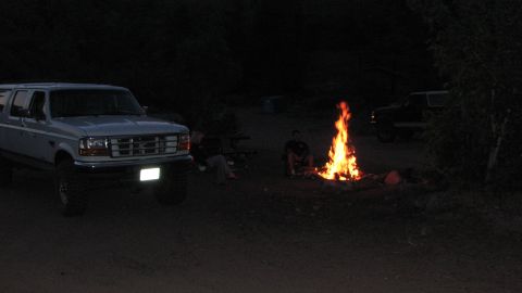 1996 Ford C-350 (Centurion Conversions) - A silver Ford Bronco is parked near a campfire with people sitting around it.