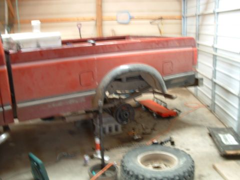 1988 Ford F-150 - The rear suspension and axle of a red pickup truck are visible while it is being worked on in a garage.