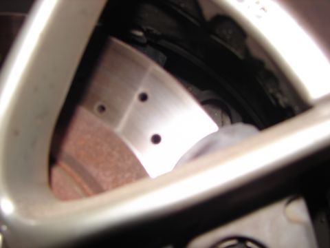 1992 Ford Taurus - Detail shot of a drilled brake rotor and caliper assembly, partially obscured by a silver alloy wheel.